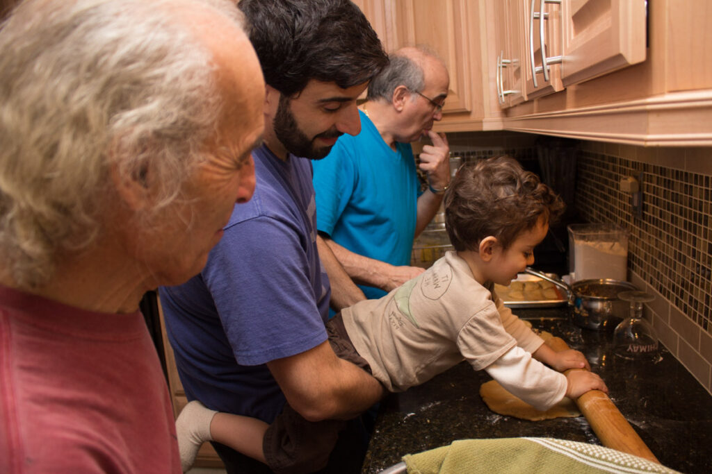 Three generations of men making cookies together in a kitchen.