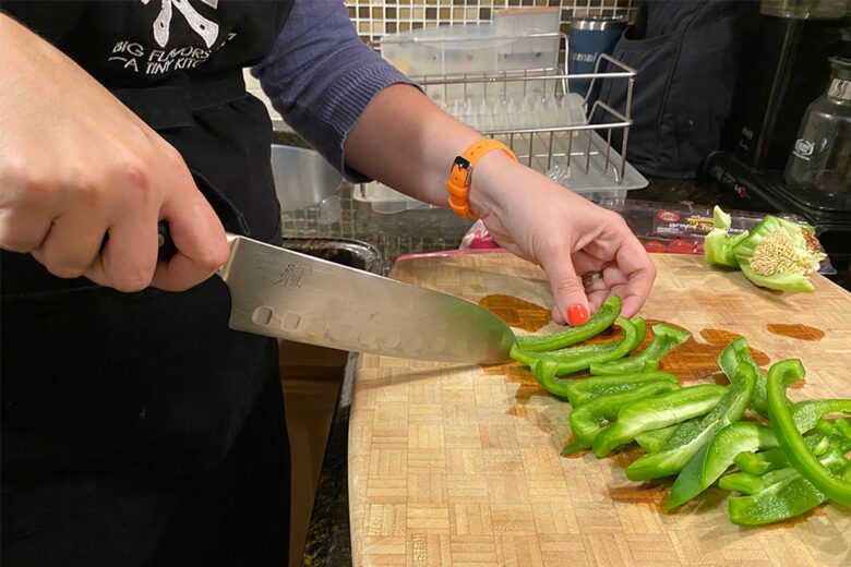 Slicing green bell peppers on a cutting board.