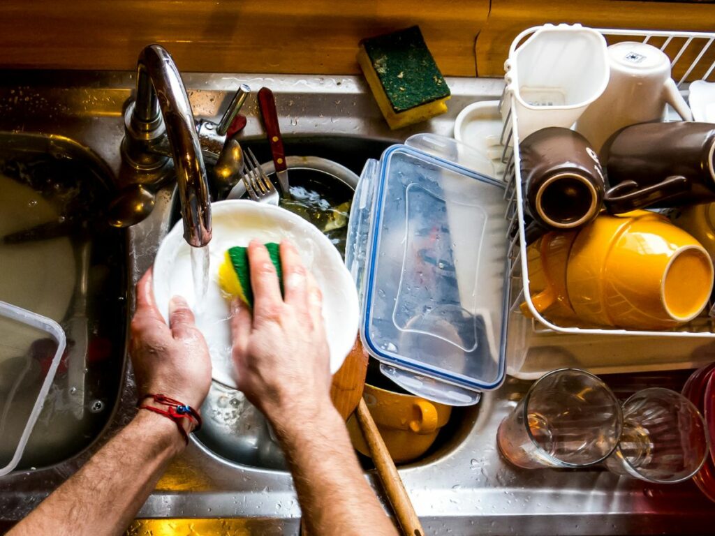 Male hands washing dishes in a sink full of dirty dishes.