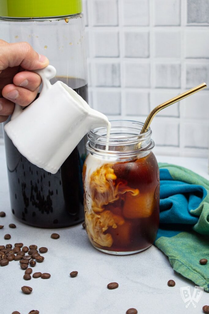 Hand pouring milk from white pitcher into cold brew coffee