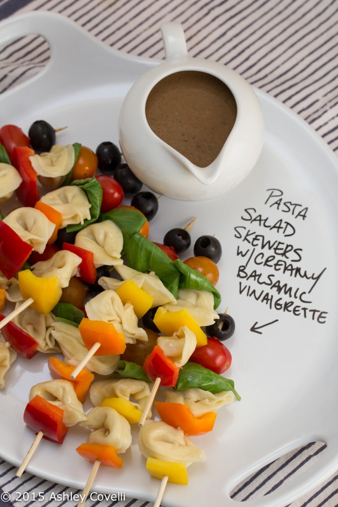 Skewers of tortellini, red peppers, basil leaves on a white plate.