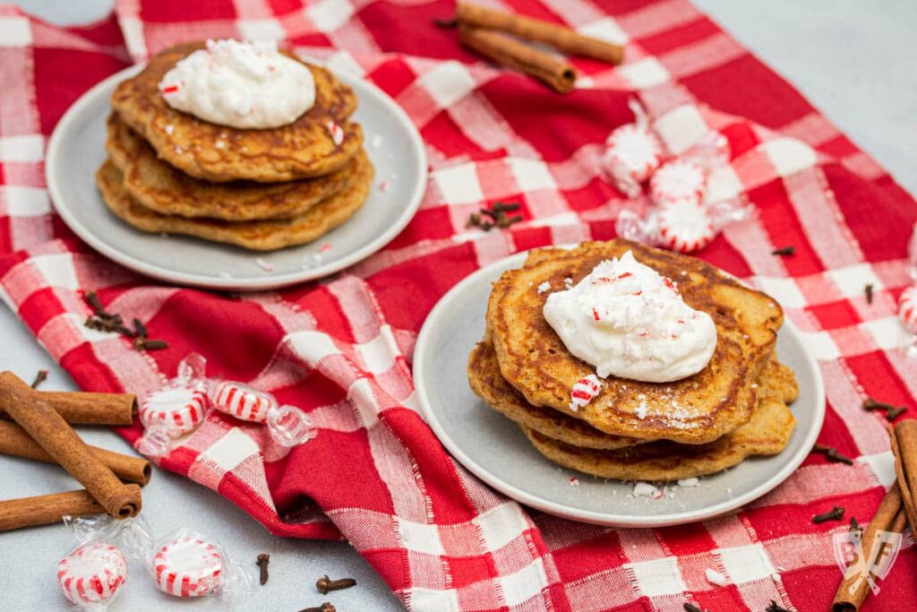 Stack of three pancakes with whipped cream and crushed peppermints on a red and white checkered dish towel.