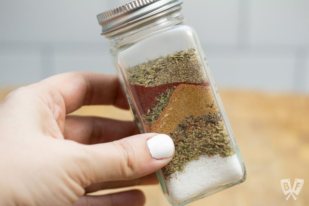 Hand holding spice bottle with layers of fajita spices.