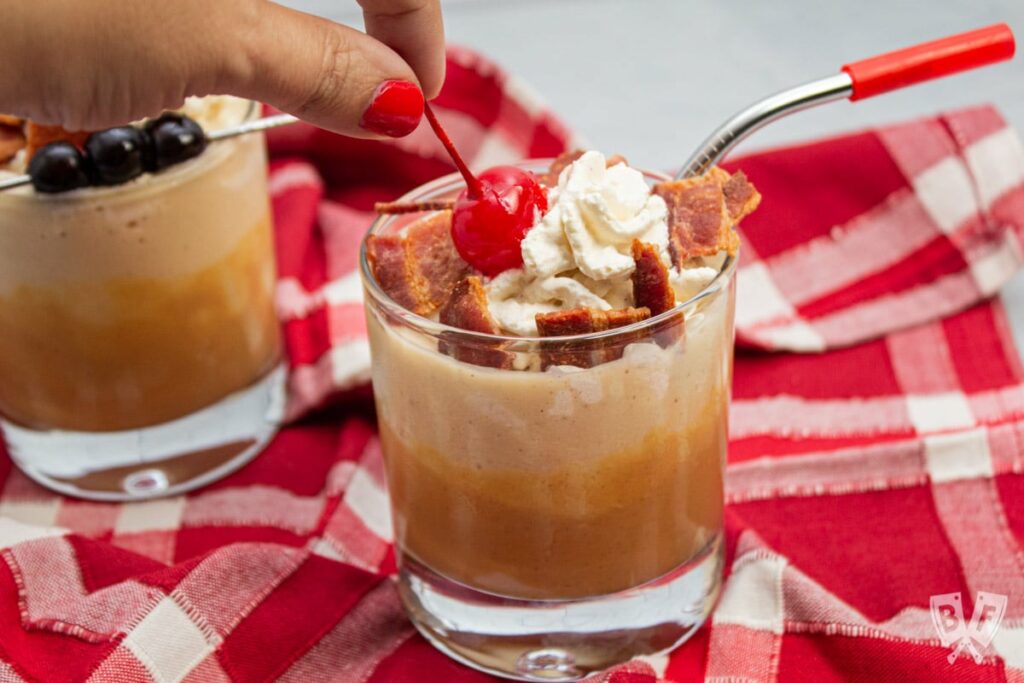 Peanut Butter banana milkshake with bacon and red cherry on top. Glass on red and white checkered towel.