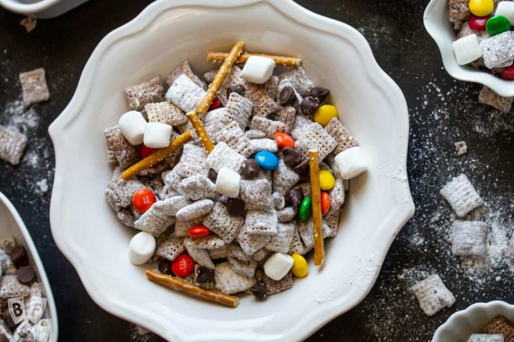 White bowl full of puppy show or muddy buddy snack mix with chex, pretzels and m and m's.