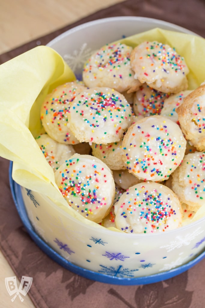 Ricotta cookies with multicolored sprinkles in a cookie tin with yellow tissue paper.