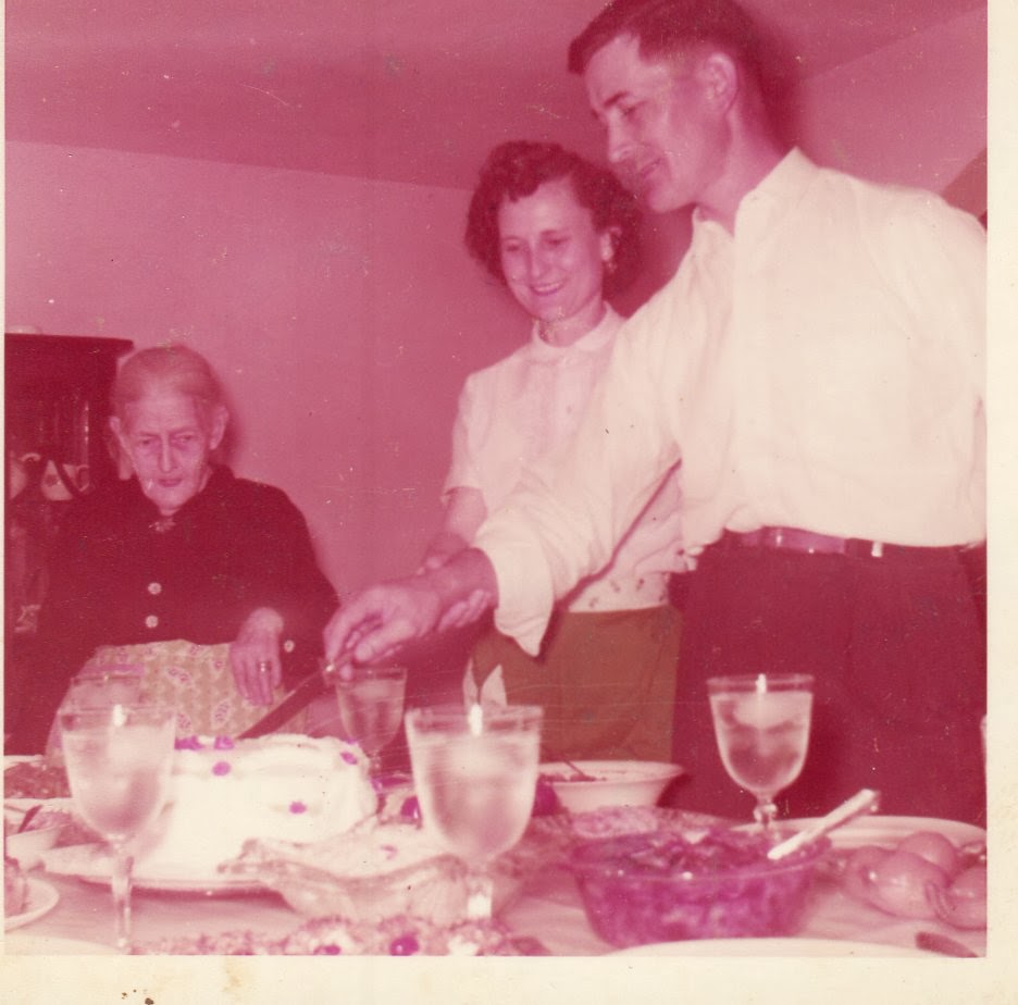 Elderly woman watching a couple cut a cake on the dinner table. 1950's.