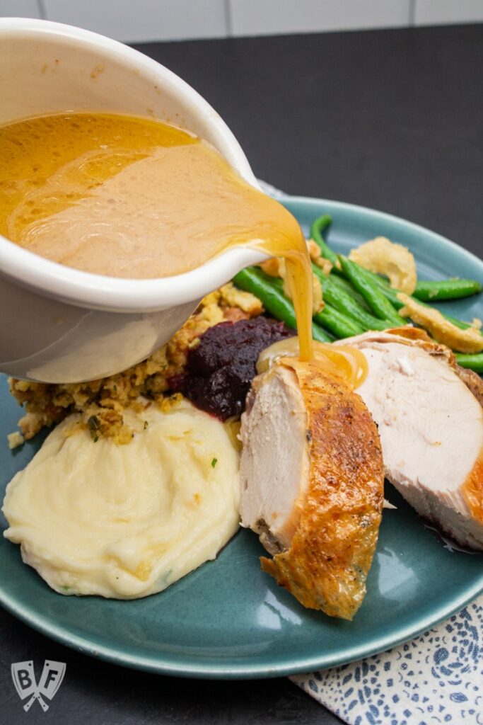 Blue plate with turkey and mashed potatoes with gravy being poured over.