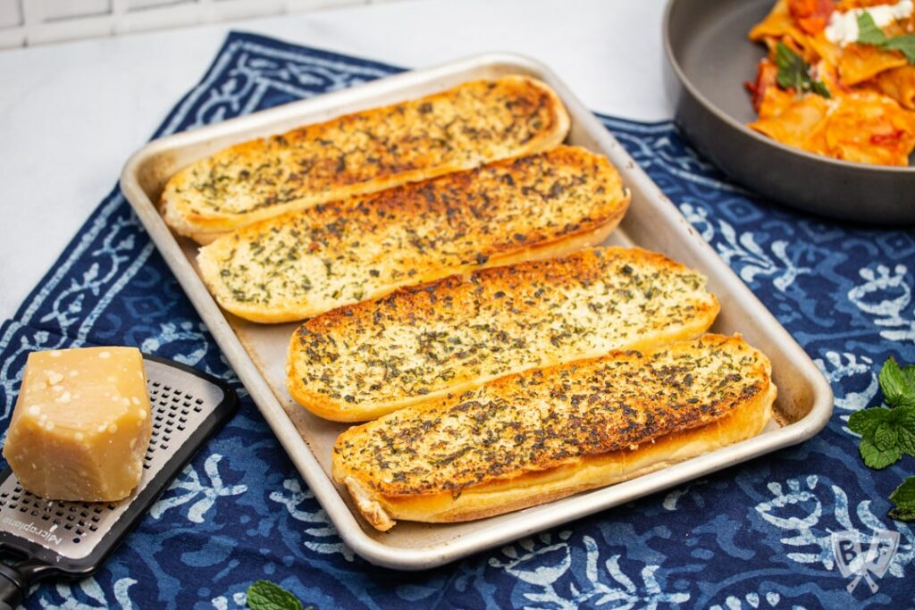 Pan with 4 slices of garlic bread on a blue tea towel