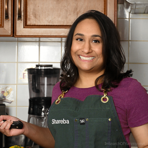 Smiling Shareba Abdul in kitchen wearing green apron.